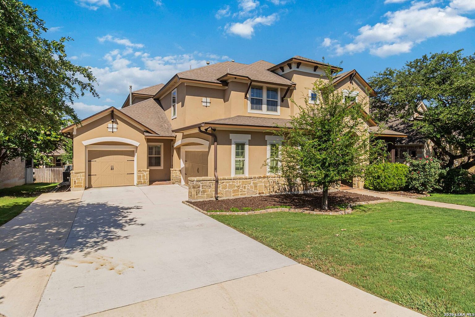 The side elevation of 28722 Front Gate showing the side-facing three-car garage, broad driveway, and the depth of the house behind a row of mature trees