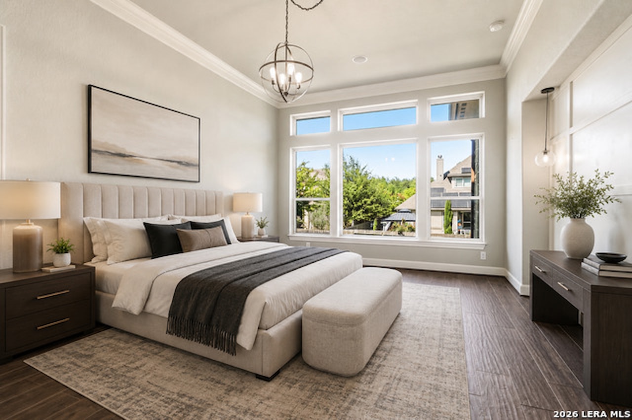 Primary bedroom at 28722 Front Gate with a channel-tufted upholstered bed, crown molding, an orb chandelier, and a bank of windows looking out to mature trees
