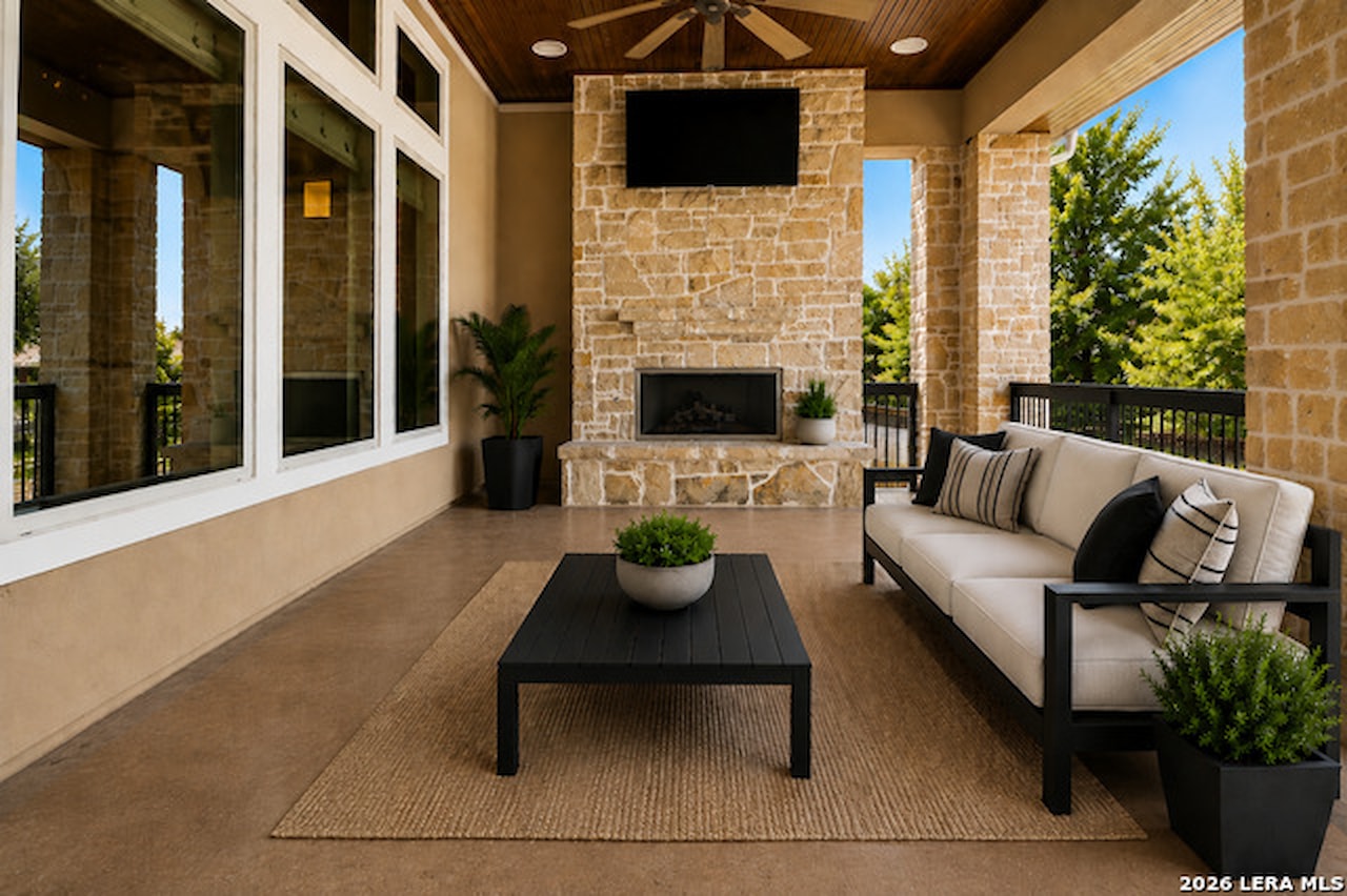 Covered patio at 28722 Front Gate with a floor-to-ceiling stone outdoor fireplace and mounted television, a wood-plank ceiling, stone columns, and outdoor seating on stained concrete