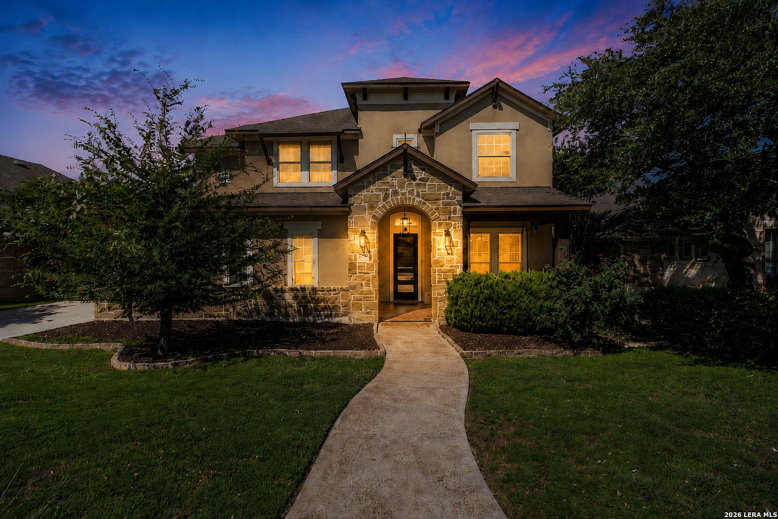 Front elevation of 28722 Front Gate at dusk, with windows warmly lit beneath a violet and rose Hill Country sky